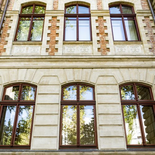 Down angle of arched windows on old beautiful building with sky and trees reflection in the glass